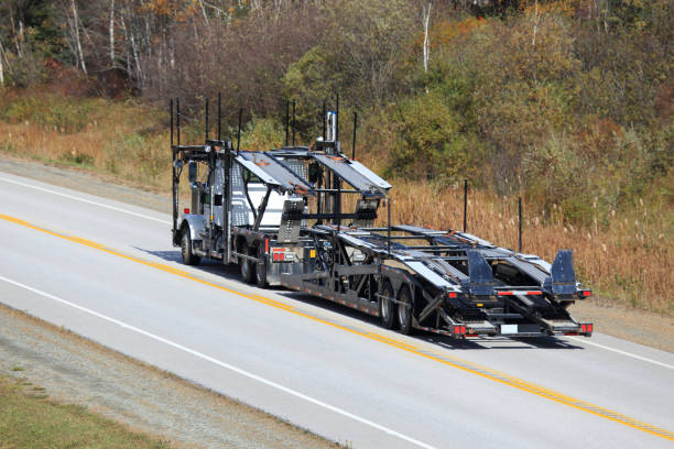 A large empty car carrier truck, part of an NC Car Shipping Concord fleet, drives along a rural two-lane road bordered by autumn trees and grass.