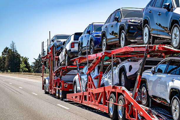 A red car carrier truck from NC Auto Transport Concord,NC, transports multiple new SUVs on a highway under a clear blue sky, with trees visible along the roadside.
